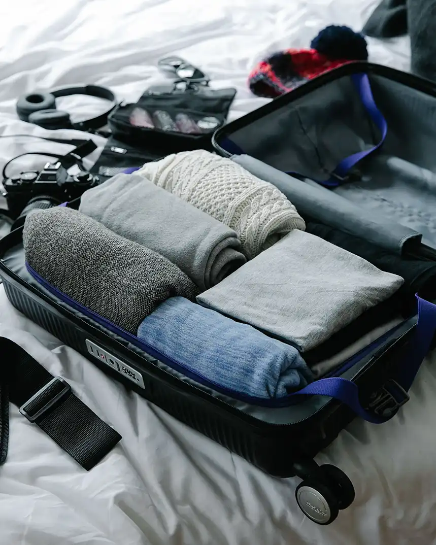 Folded knitwear and other clothes arranged inside an open suitcase on a bed