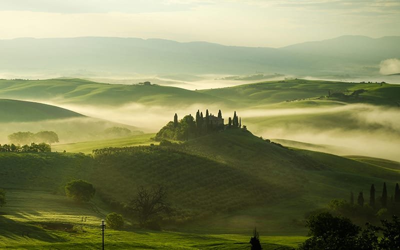 Trip to Italy - a green rolling hills with fog and a house on top