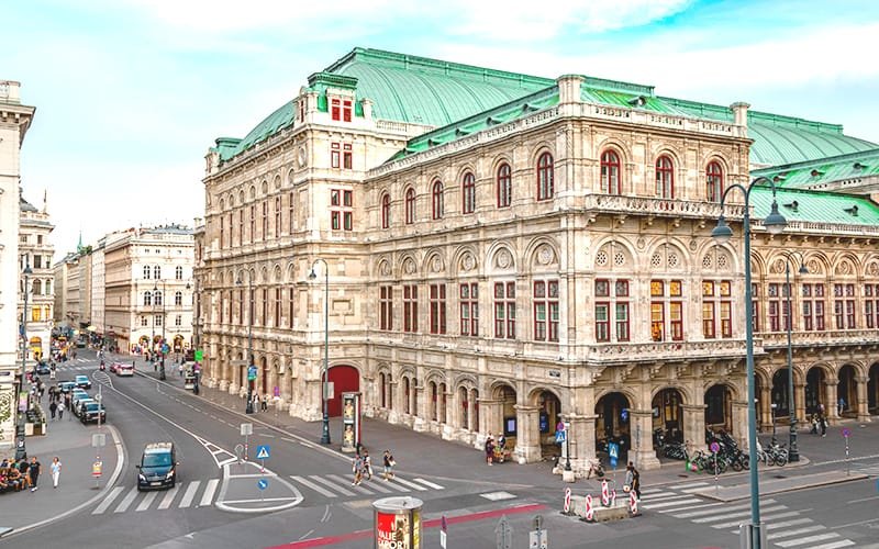 a large stone building with many windows and a green roof with Vienna State Opera in the background