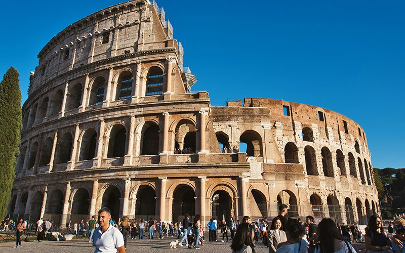 city breaks - a group of people walking around a large circular building with Colosseum in the background