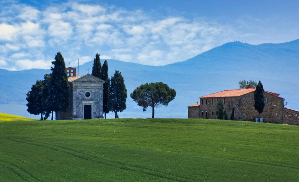 a stone building in a field with trees and mountains in the background