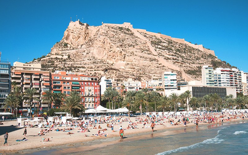 a beach with a large hill and buildings